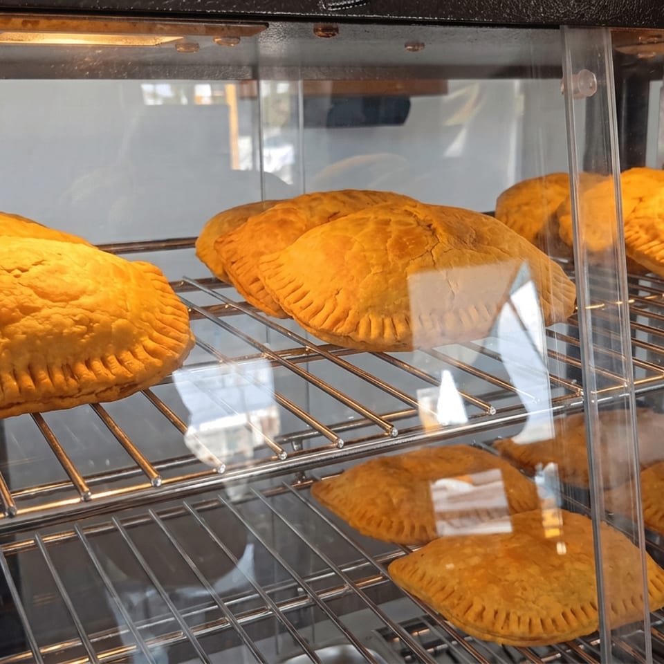 Golden-brown handmade empanadas arranged on wire racks inside a glass-fronted warming display case.