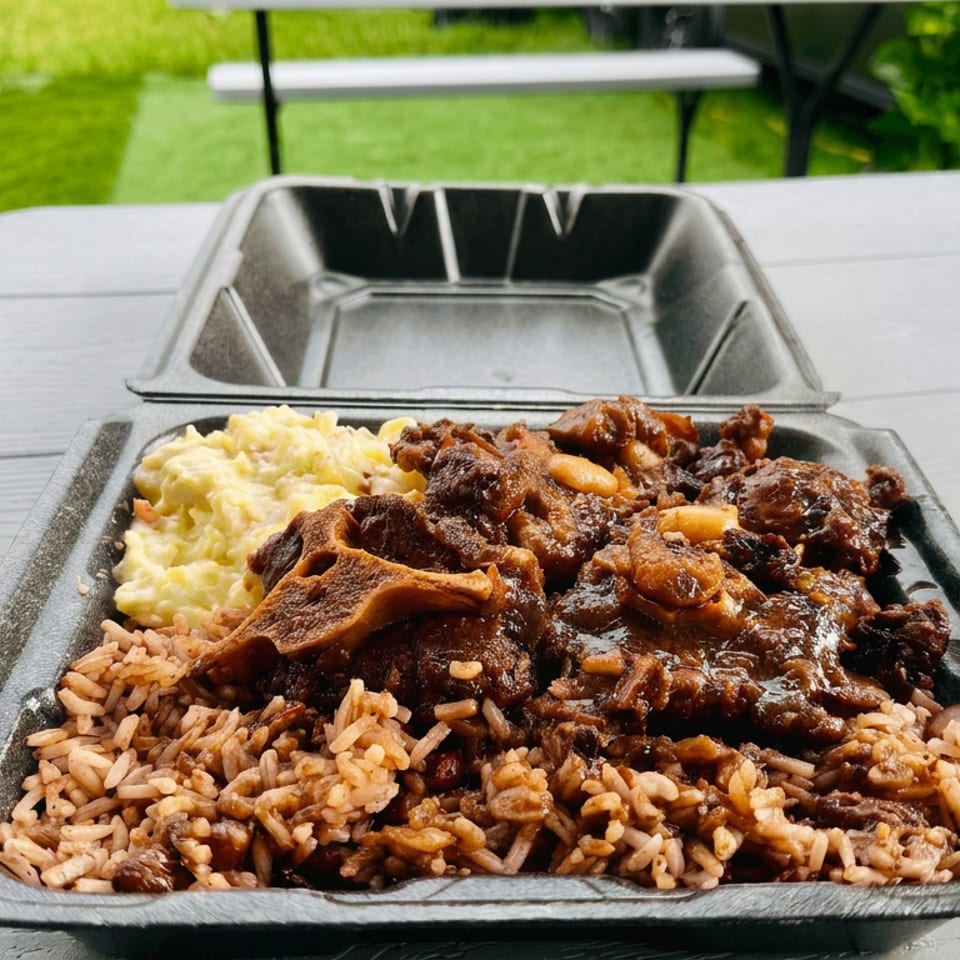 Tray of seasoned rice, creamy coleslaw, and saucy braised meat on an outdoor picnic table.